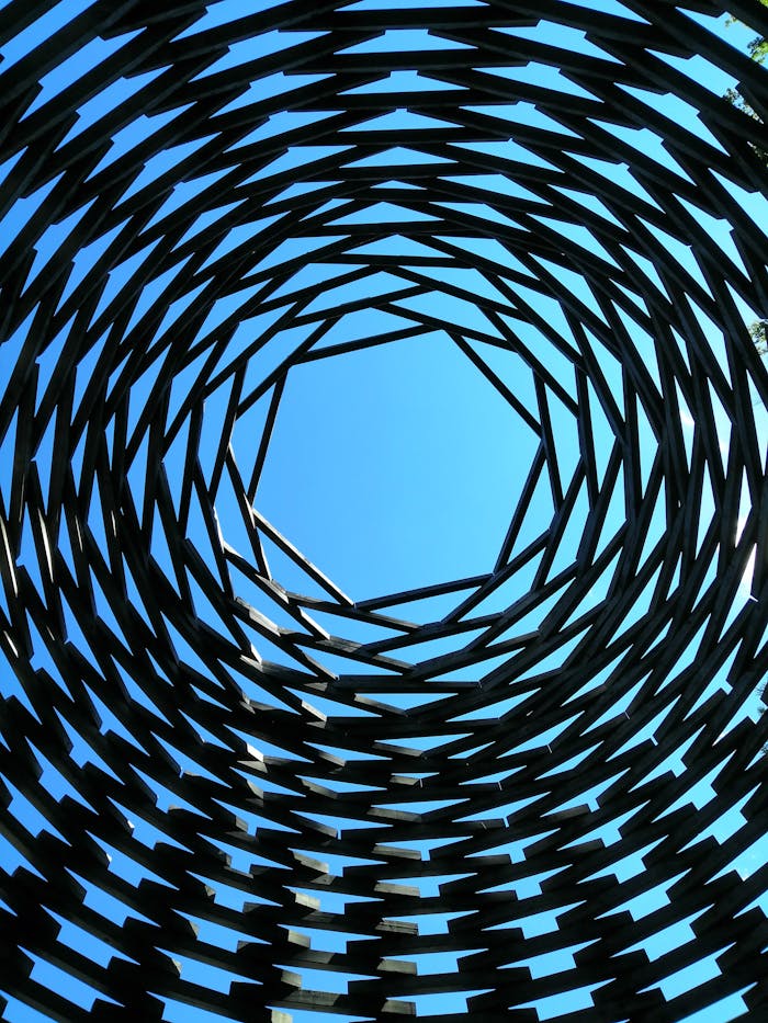 A mesmerizing geometric spiral structure leading the eye to a bright blue sky.